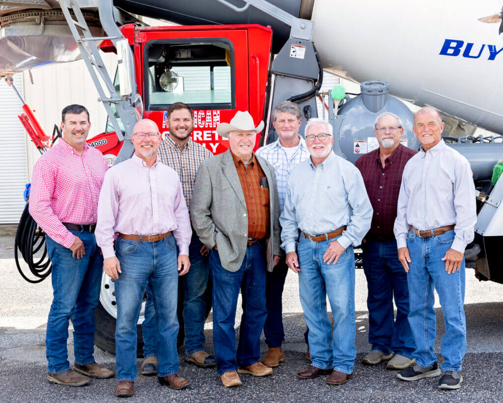 A group of men standing in front of a concrete mixer truck, representing team members and leadership in construction industry careers
