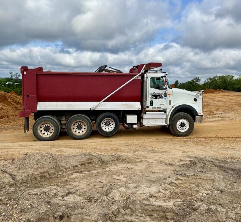 A red and white dump truck parked on a construction site, used for hauling dirt or construction materials.