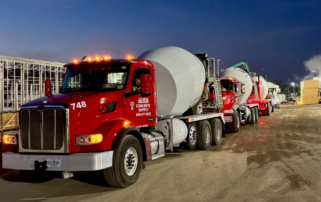 A row of red concrete mixer trucks lined up at an industrial construction site during early morning hours.