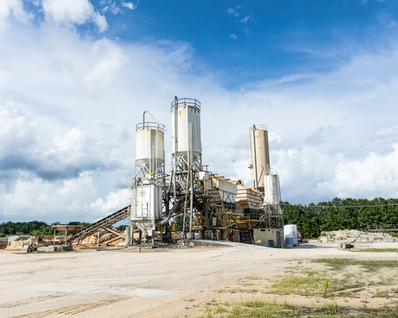 An industrial concrete batching plant with silos and conveyor systems, providing concrete mixing and supply services.