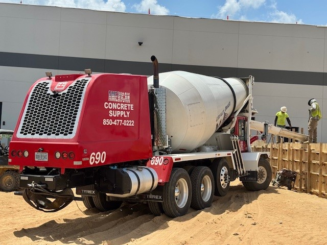 Concrete mixer truck from Concrete Supply (850-477-0222) delivering concrete at a construction site with workers preparing a wooden form. Blog image.